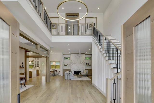 entryway with recessed lighting, a towering ceiling, a premium fireplace, wood finished floors, and stairs