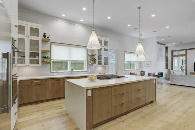 kitchen featuring a spacious island, sink, decorative light fixtures, light wood-type flooring, and stainless steel gas stovetop