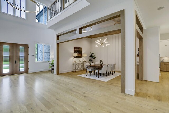 entryway with a towering ceiling, an inviting chandelier, light wood-type flooring, and french doors