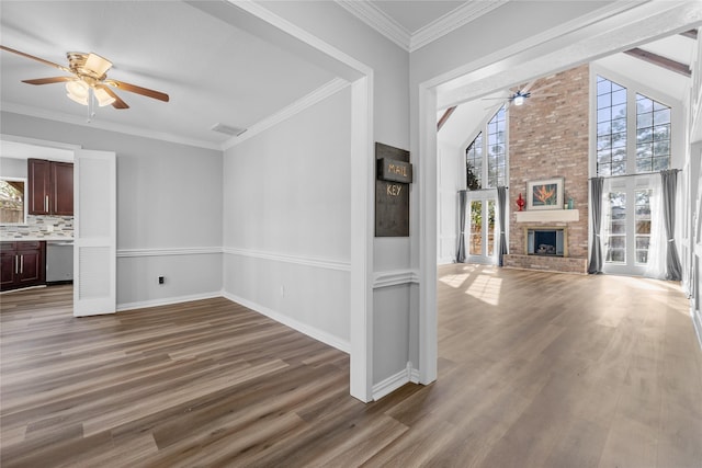 unfurnished living room featuring wood-type flooring, a brick fireplace, ornamental molding, and ceiling fan