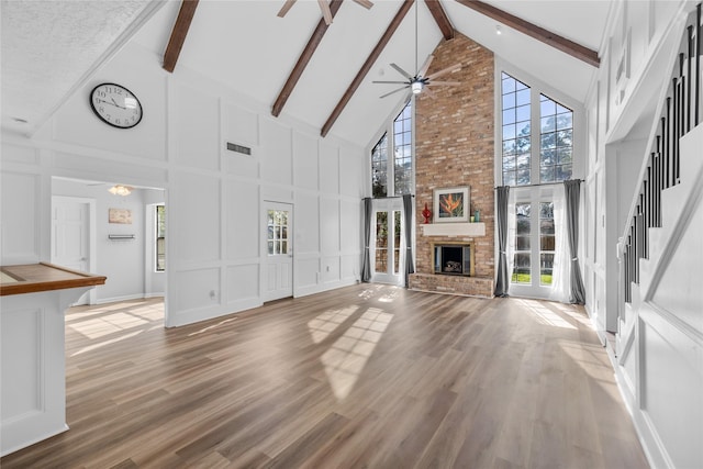 unfurnished living room with ceiling fan, wood-type flooring, beam ceiling, and a brick fireplace