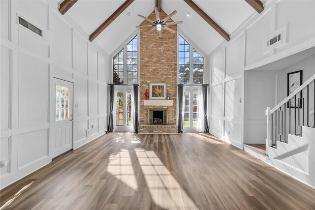 unfurnished living room featuring high vaulted ceiling, beamed ceiling, hardwood / wood-style flooring, ceiling fan, and a brick fireplace