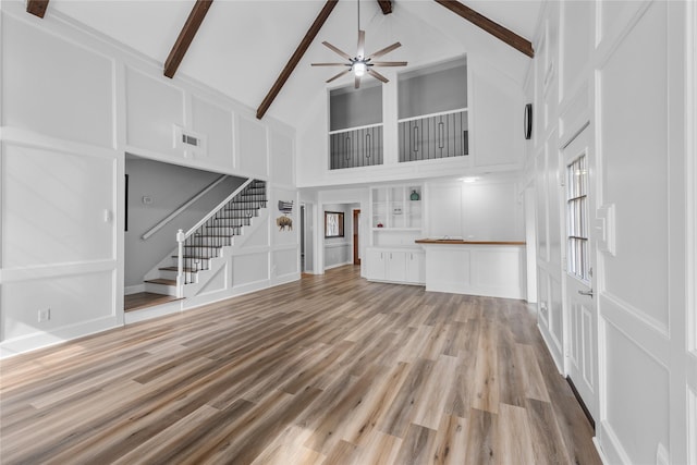 unfurnished living room with beamed ceiling, ceiling fan, high vaulted ceiling, and light wood-type flooring