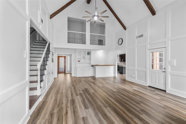 unfurnished living room with high vaulted ceiling, built in features, ceiling fan, beam ceiling, and hardwood / wood-style floors