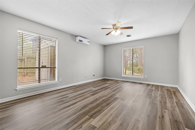 spare room with ceiling fan, hardwood / wood-style floors, a textured ceiling, and a wall unit AC