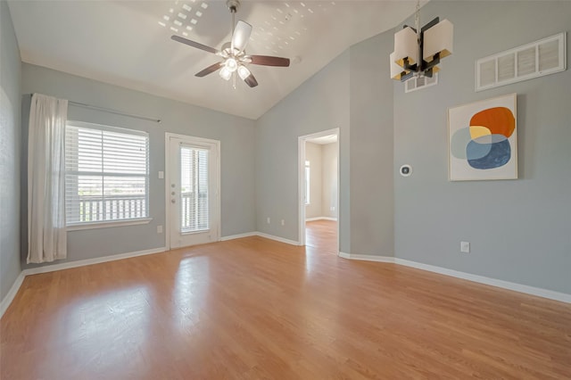 spare room featuring lofted ceiling, ceiling fan with notable chandelier, and light wood-type flooring