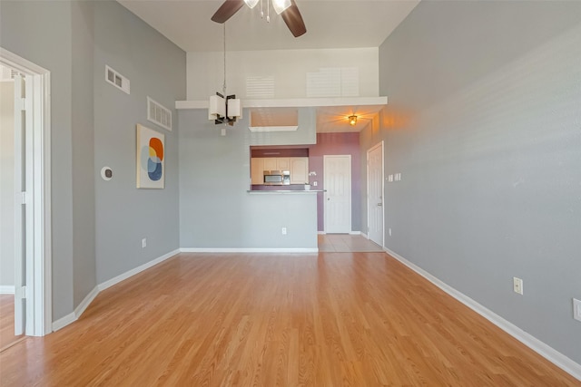 unfurnished living room with ceiling fan with notable chandelier, light hardwood / wood-style floors, and a high ceiling