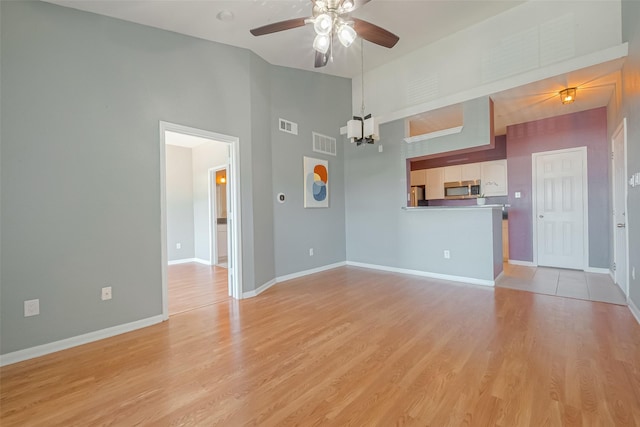 unfurnished living room with ceiling fan with notable chandelier, high vaulted ceiling, and light hardwood / wood-style floors