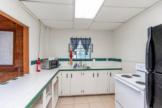 kitchen with electric stove, sink, tile counters, white cabinets, and black fridge