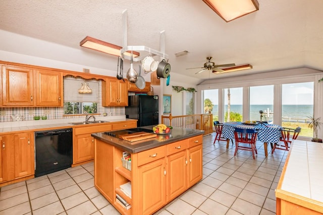 kitchen with vaulted ceiling, tile countertops, a center island, black appliances, and a water view