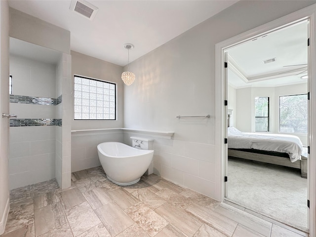 bathroom with visible vents, ensuite bathroom, walk in shower, a freestanding bath, and tile walls