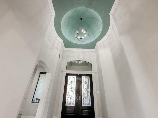 entryway featuring arched walkways, french doors, a towering ceiling, an inviting chandelier, and ornamental molding