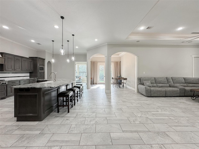 kitchen with arched walkways, light stone counters, a kitchen breakfast bar, open floor plan, and an island with sink