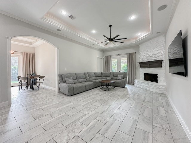 living room featuring a tray ceiling, arched walkways, crown molding, visible vents, and a stone fireplace