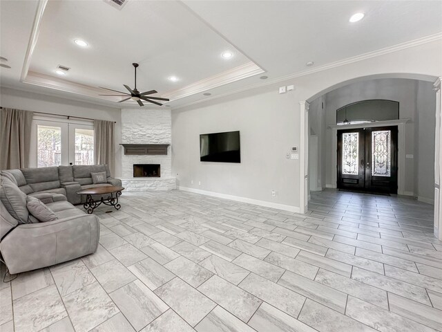 unfurnished living room featuring crown molding, a stone fireplace, a tray ceiling, and french doors