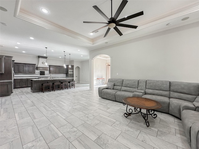 living area with arched walkways, recessed lighting, a raised ceiling, ornamental molding, and ceiling fan