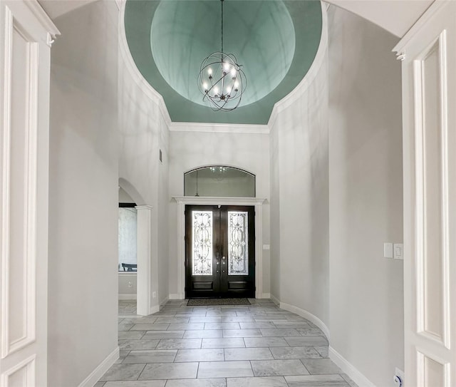 foyer with an inviting chandelier, a towering ceiling, and french doors