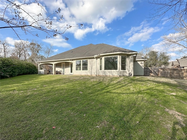 rear view of property with a shingled roof, stucco siding, fence, and a lawn