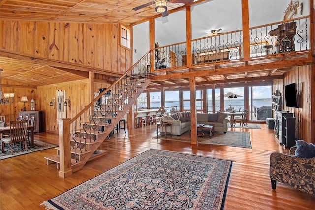 living area featuring ceiling fan with notable chandelier, a towering ceiling, wood walls, wood finished floors, and stairs