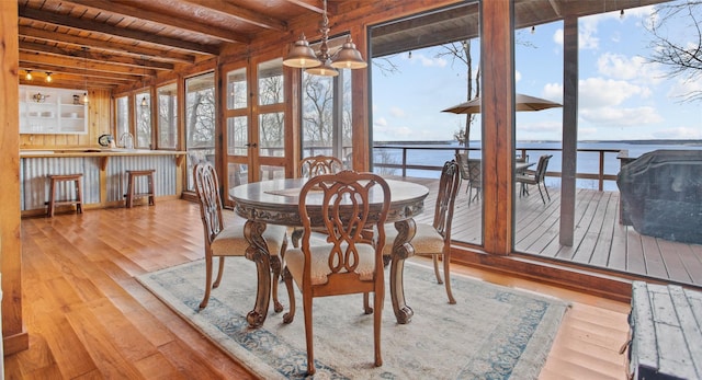 dining space with wood ceiling, beamed ceiling, a water view, french doors, and light wood-style floors