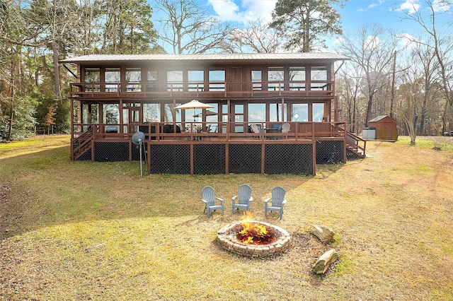 rear view of property with a sunroom, a fire pit, a wooden deck, and a storage shed