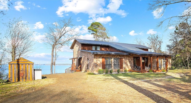 back of property featuring a storage shed, metal roof, a water view, a yard, and an outdoor structure