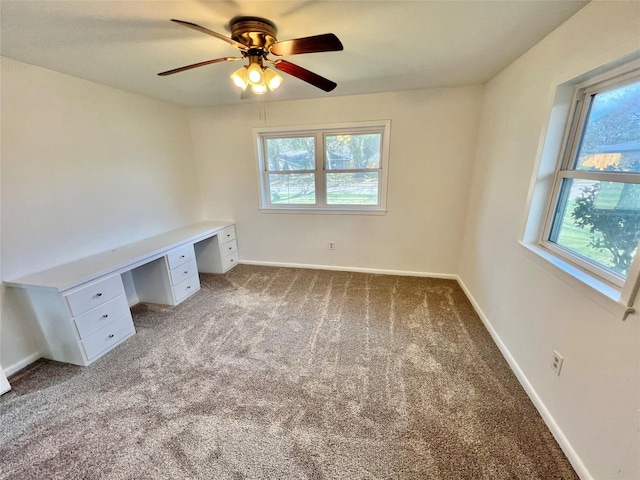 unfurnished office with ceiling fan, light colored carpet, plenty of natural light, and built in desk