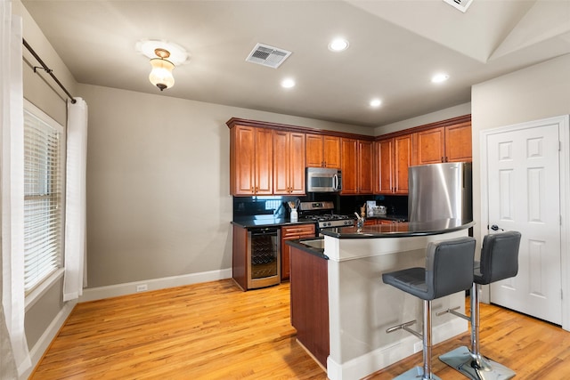 kitchen with appliances with stainless steel finishes, a breakfast bar, beverage cooler, and light wood-type flooring