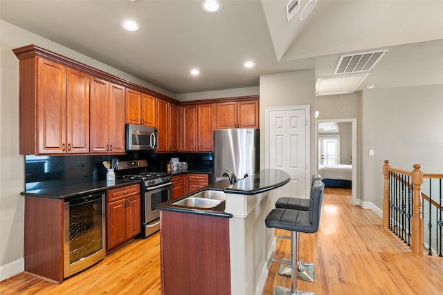 kitchen with stainless steel appliances, an island with sink, beverage cooler, and light hardwood / wood-style flooring