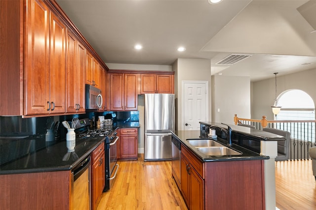 kitchen featuring appliances with stainless steel finishes, sink, hanging light fixtures, a center island with sink, and light wood-type flooring