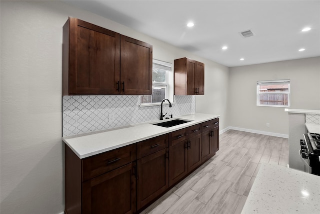 kitchen with sink, dark brown cabinets, light hardwood / wood-style floors, light stone countertops, and decorative backsplash