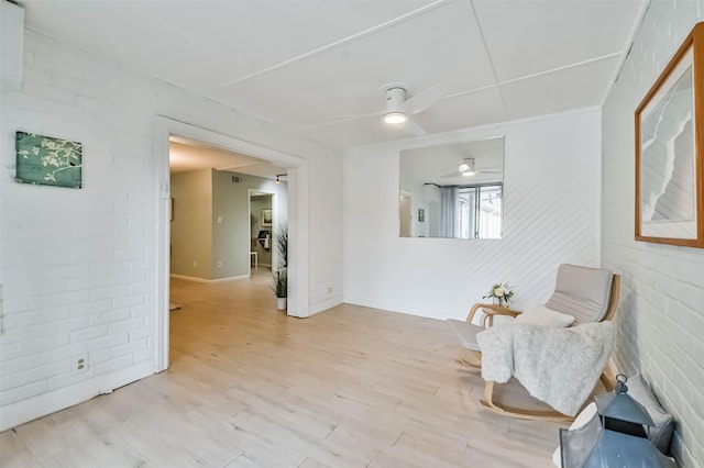 living area with light hardwood / wood-style flooring, ceiling fan, and brick wall