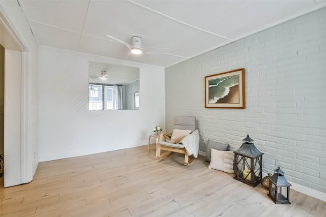 living area with ceiling fan, brick wall, and light wood-type flooring