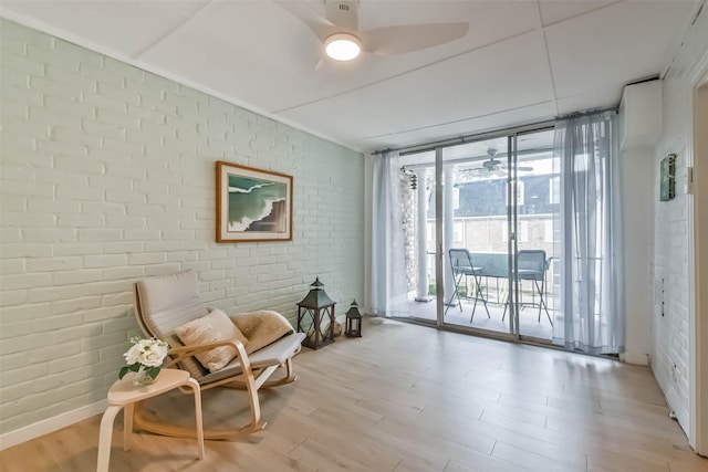 living area with light wood-type flooring, expansive windows, ceiling fan, and brick wall