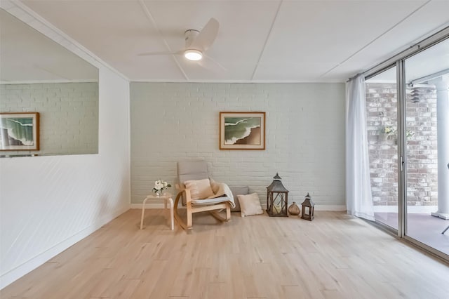 living area with ceiling fan, brick wall, and light hardwood / wood-style floors