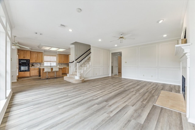 unfurnished living room with crown molding, ceiling fan, and light hardwood / wood-style flooring