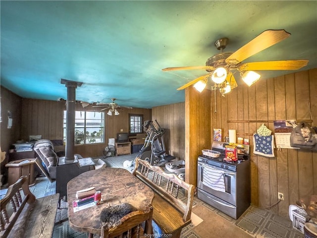 kitchen featuring stainless steel stove, wooden walls, ceiling fan, and a wood stove