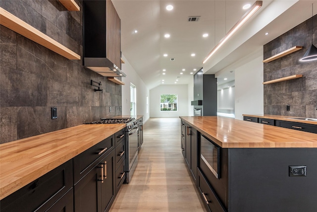 kitchen featuring black microwave, butcher block counters, backsplash, a center island, and stainless steel gas range