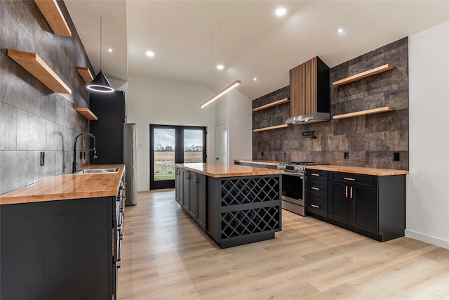 kitchen featuring appliances with stainless steel finishes, pendant lighting, wall chimney range hood, and wooden counters