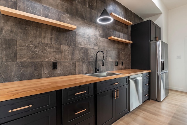 kitchen featuring appliances with stainless steel finishes, tasteful backsplash, butcher block counters, sink, and light wood-type flooring