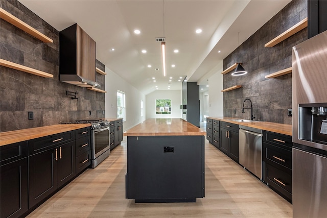 kitchen featuring a kitchen island, sink, wooden counters, stainless steel appliances, and wall chimney exhaust hood