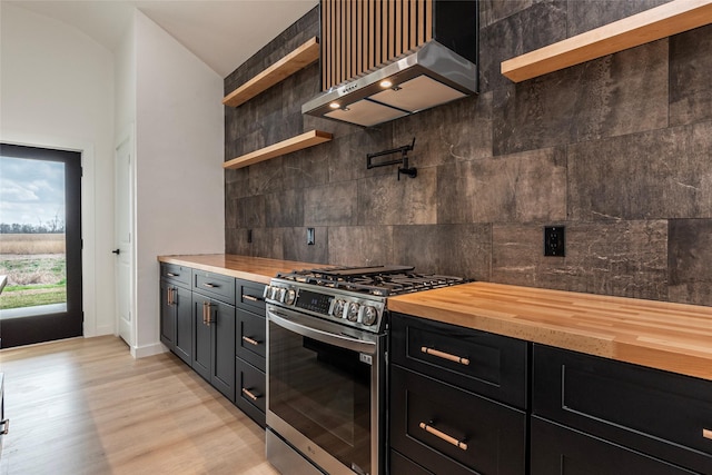 kitchen with stainless steel range with gas cooktop, decorative backsplash, butcher block countertops, and wall chimney exhaust hood