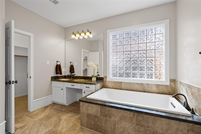 bathroom with vanity, a healthy amount of sunlight, and a relaxing tiled tub