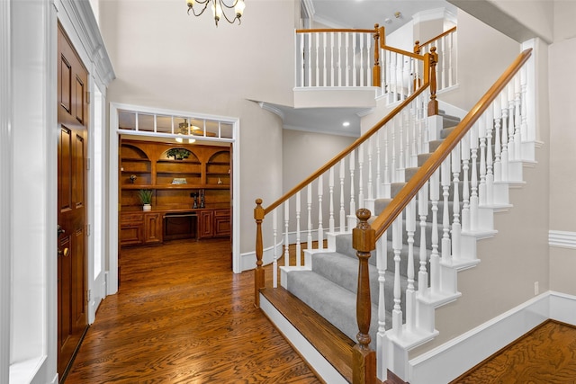 entrance foyer with wood-type flooring, a towering ceiling, a notable chandelier, and ornamental molding