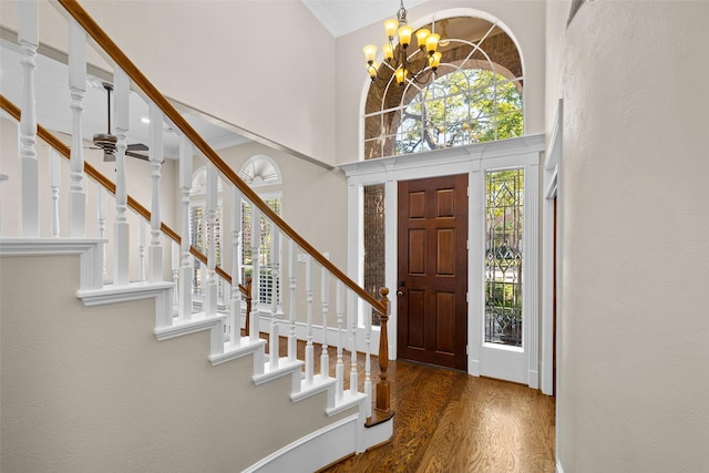 entryway with crown molding, dark hardwood / wood-style floors, ceiling fan with notable chandelier, and a towering ceiling