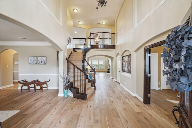 foyer entrance featuring arched walkways, light wood-style flooring, stairway, and a towering ceiling