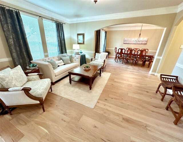 living room featuring light wood-style floors, arched walkways, a notable chandelier, and ornamental molding