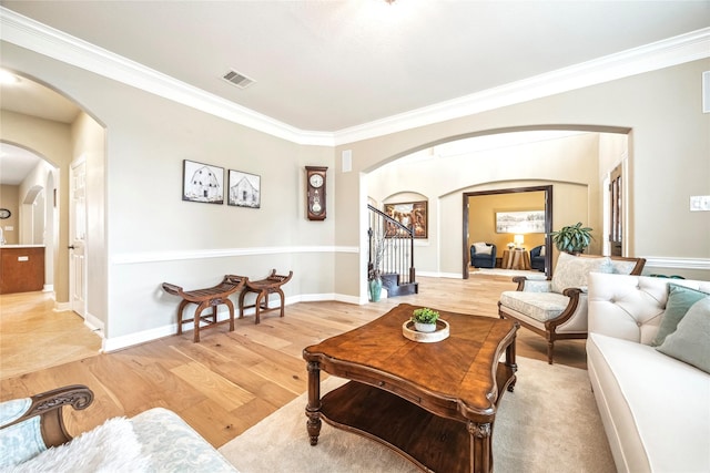 living room featuring arched walkways, light wood-style flooring, visible vents, stairs, and crown molding