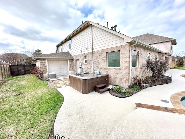 rear view of house with fence, a hot tub, brick siding, a lawn, and a patio