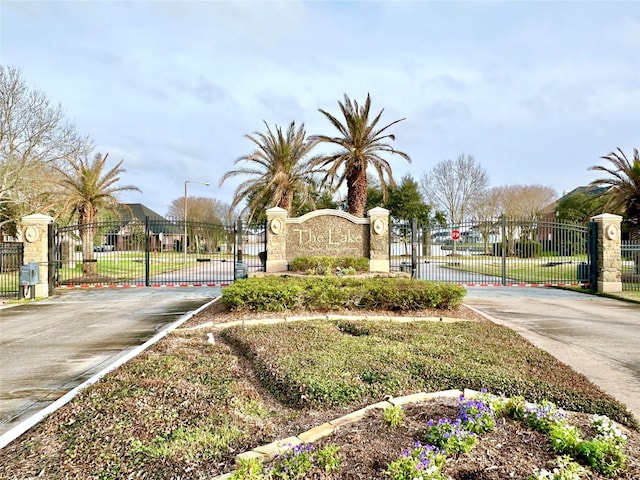 community / neighborhood sign featuring fence, a gate, and concrete driveway